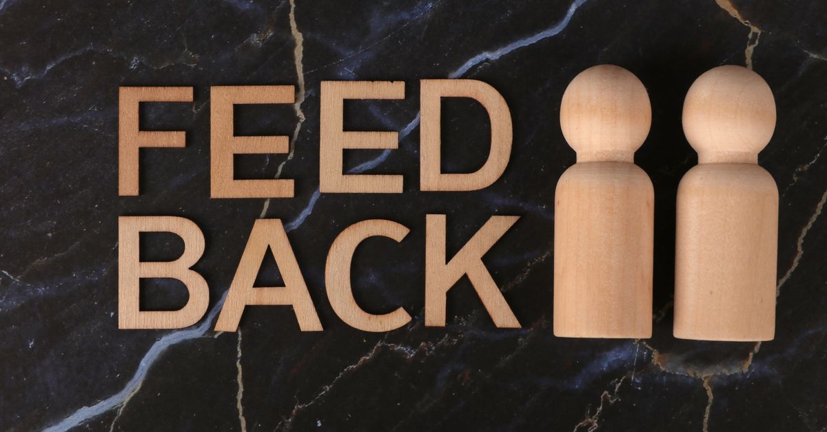 Wooden figures and 'feedback' text on black marble background, symbolizing communication and review.
