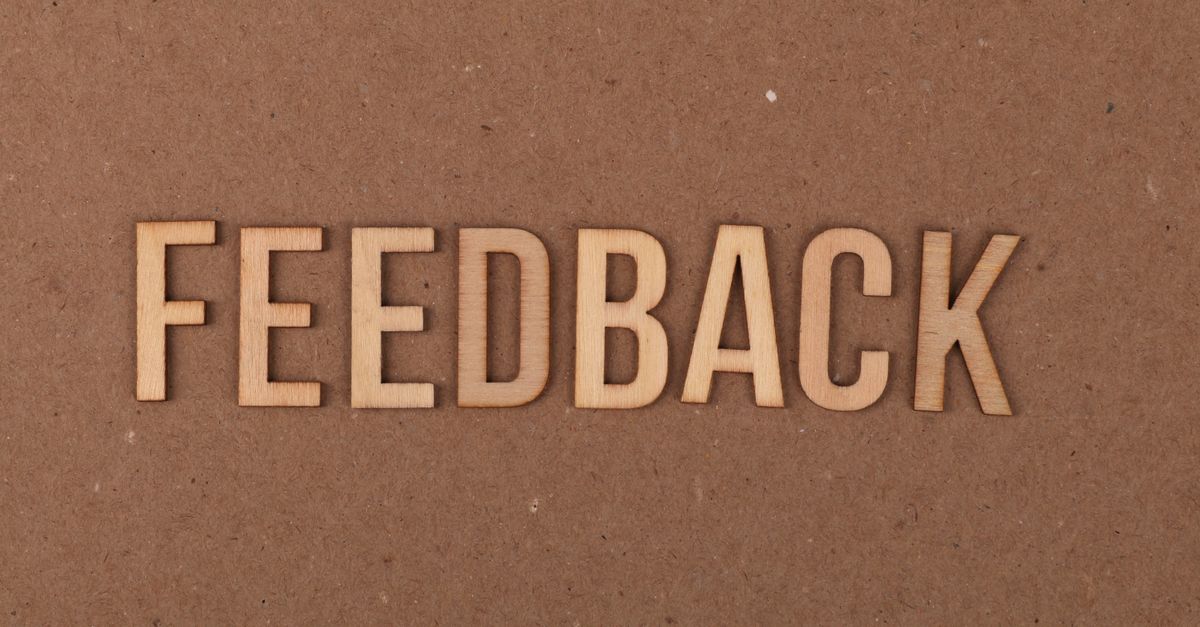 A close-up of a wooden 'FEEDBACK' sign on a textured cardboard background.