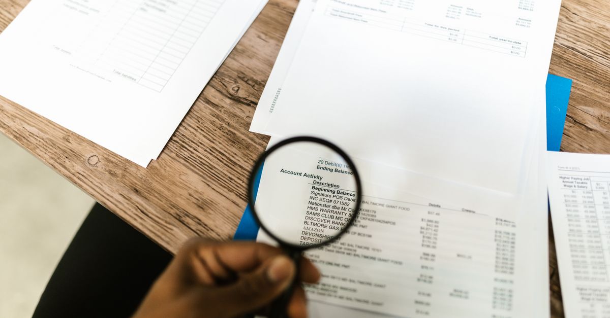 Close-up of hand using magnifying glass to review documents. Ideal for financial themes.