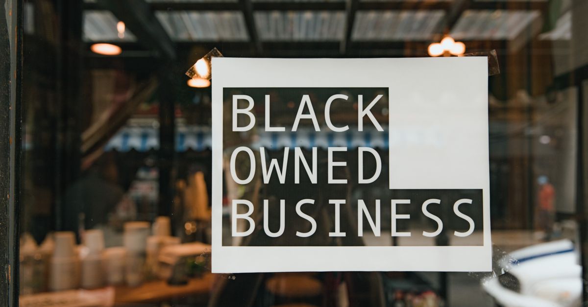 Black owned business sign taped on a window, seen from outside a store.