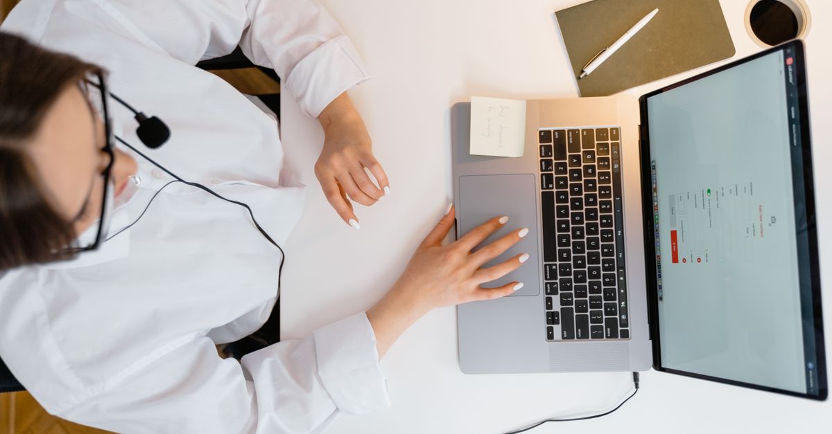 A call center agent wearing a headset works on her laptop in a bright, modern office.