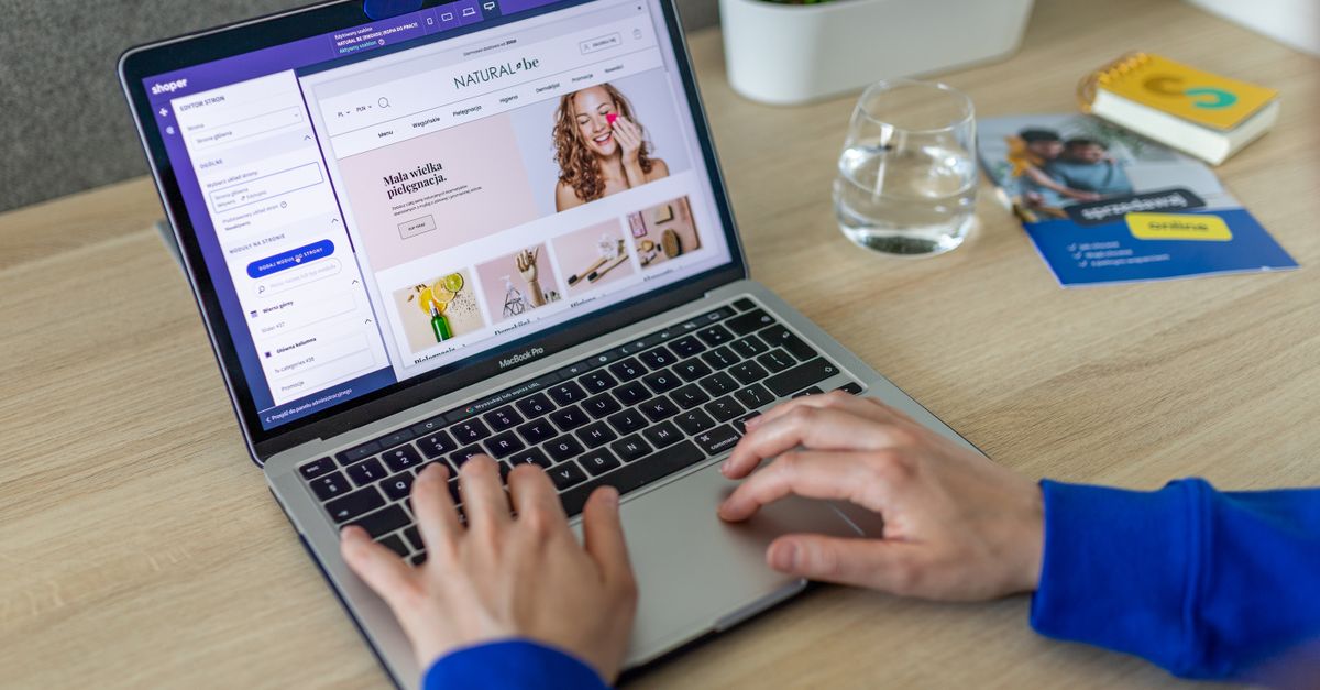 Hands typing on a laptop showing an e-commerce website in a modern office setting.