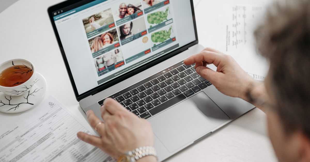 A person browsing a website on a laptop with a cup of tea and documents on a table.