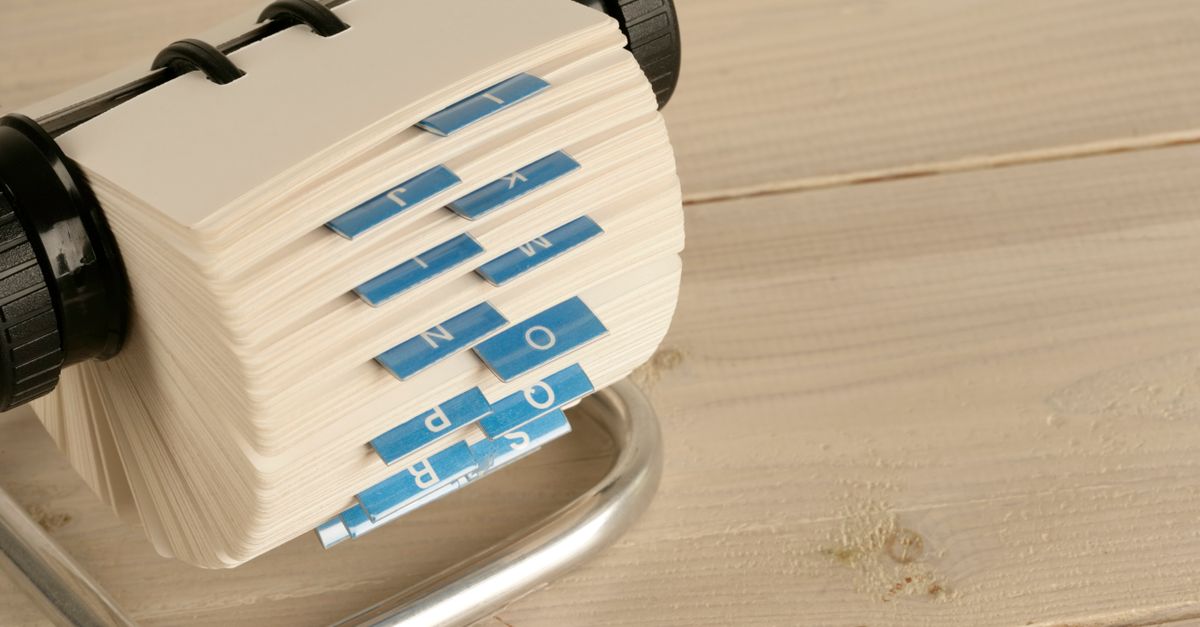 A close-up of a traditional Rolodex with alphabet tabs on a wooden desk.