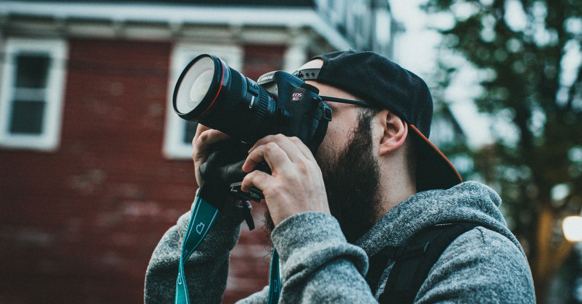 A bearded man photographer capturing a scene outdoors with a DSLR camera.
