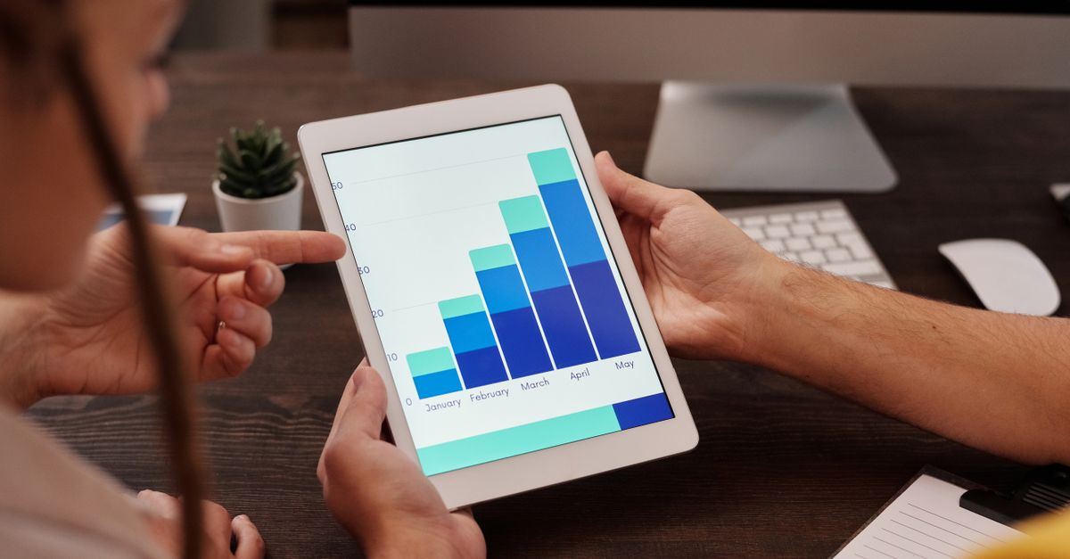 Two adults working in an office, examining graphs on a tablet screen for data analysis.