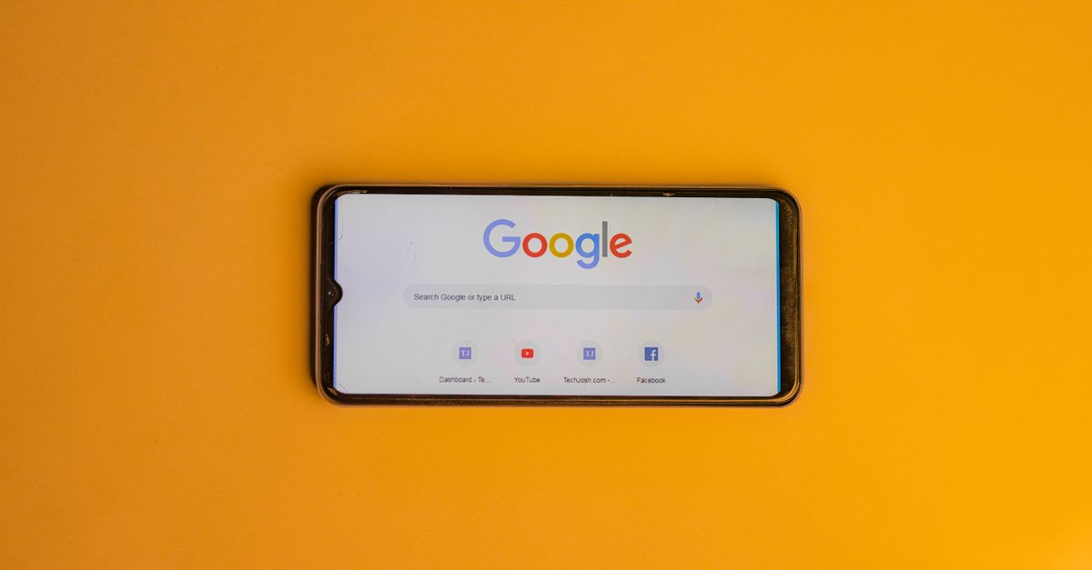 Smartphone displaying Google search page on a vibrant yellow background.