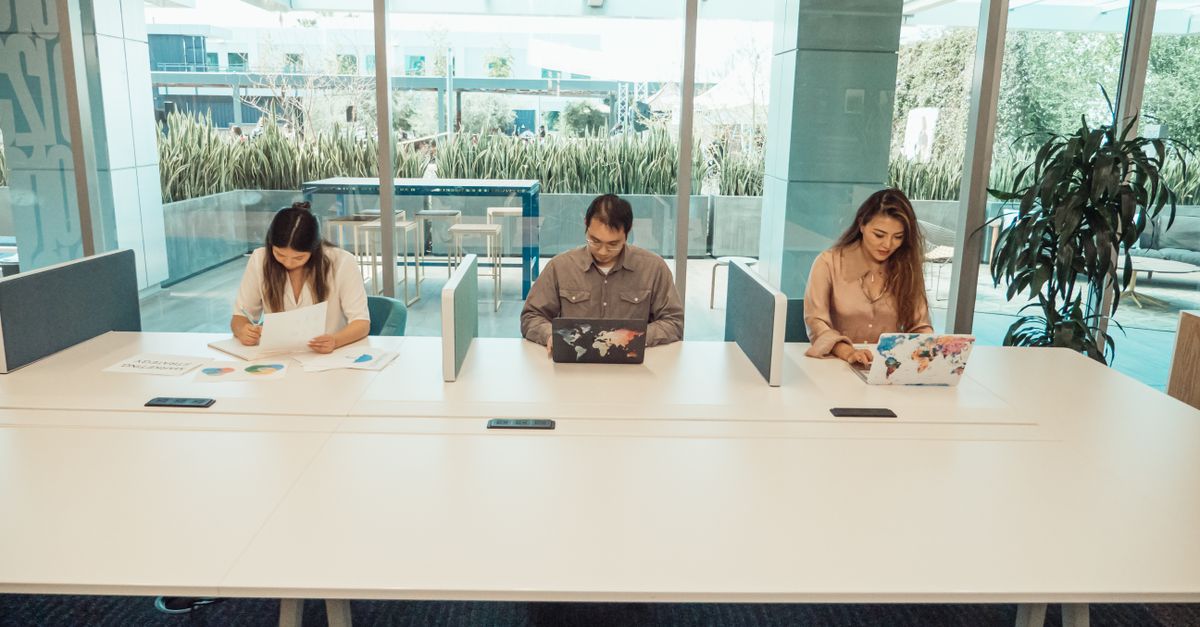Three professionals collaborating in a modern office space with laptops and documents.