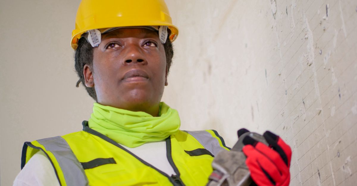 Portrait of a female construction worker in safety gear holding a wrench indoors.