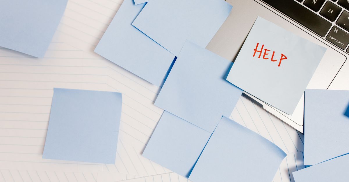 A cluttered workspace with sticky notes on a laptop, symbolizing overwhelm and need for help.