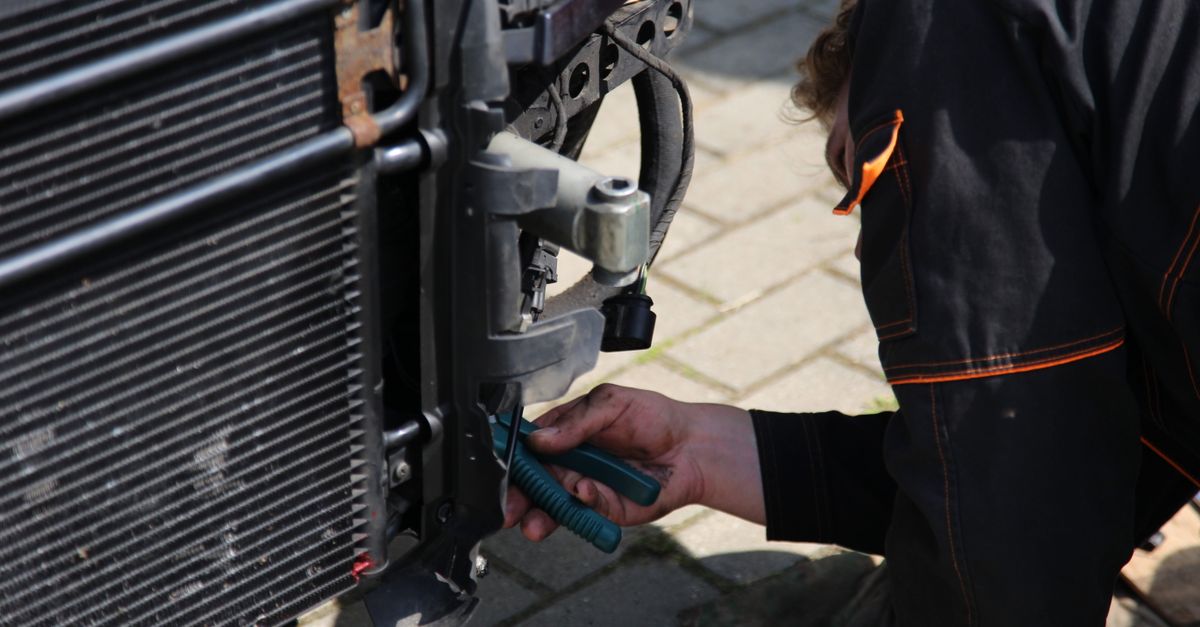 Mechanic working on car repair outdoors using tools, focusing on vehicle radiator area.