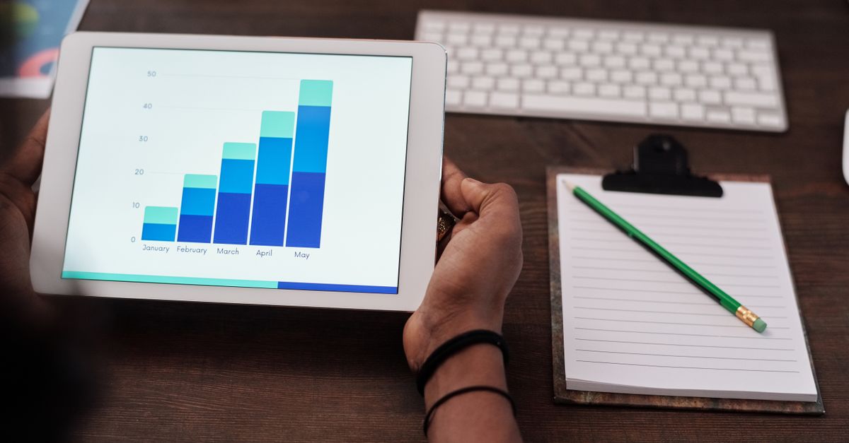 Close-up of a person holding a tablet showing growth charts on a wooden desk setup.