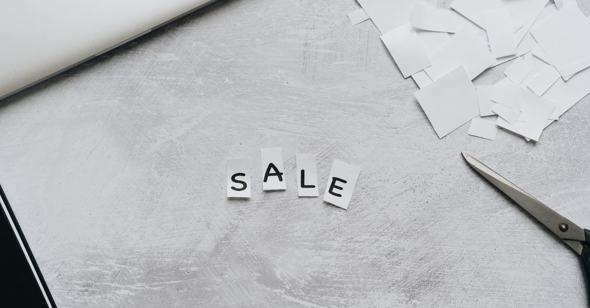 Overhead view of cut-out letters spelling 'Sale' on a desk with scattered paper and scissors.
