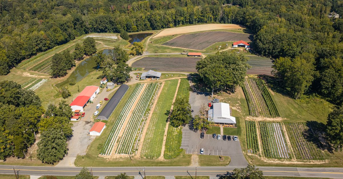 Expansive aerial view of farmland in North Carolina with fields, buildings, and natural surroundings.