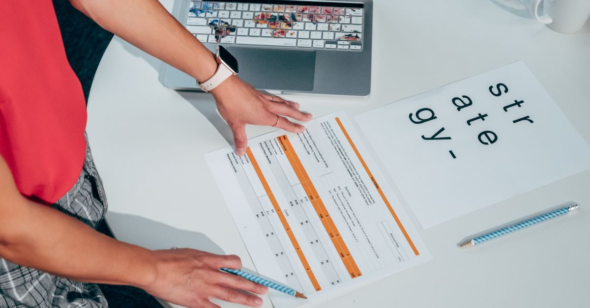 Top view of a person strategizing with documents and a laptop on a table.