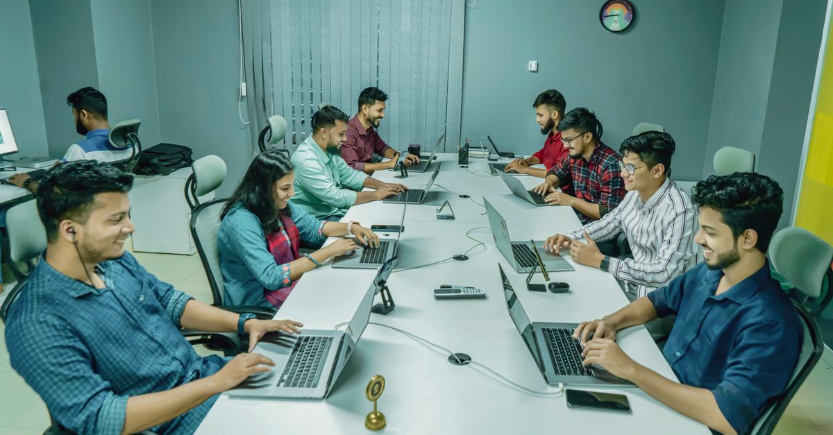 Group of professionals collaborating in a modern office setting on laptops and digital devices.
