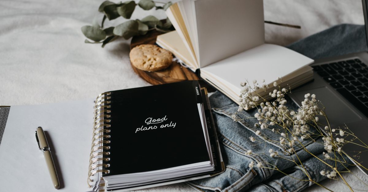 Aesthetic workspace with a notebook, pen, flowers, and laptop on a cozy surface.