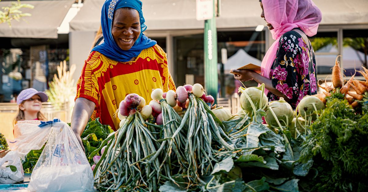 Two women engage in friendly commerce at a colorful outdoor vegetable market.