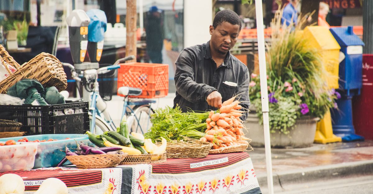 Man arranging fresh vegetables at an outdoor street market stall.