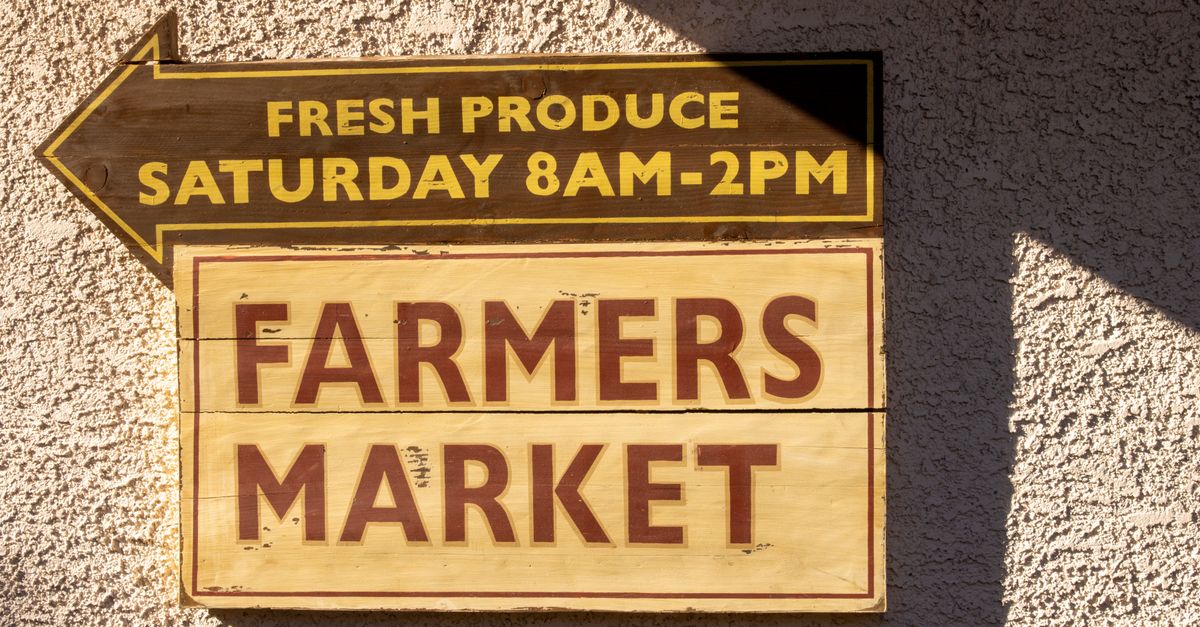 Brightly painted farmers market sign indicating fresh produce times.