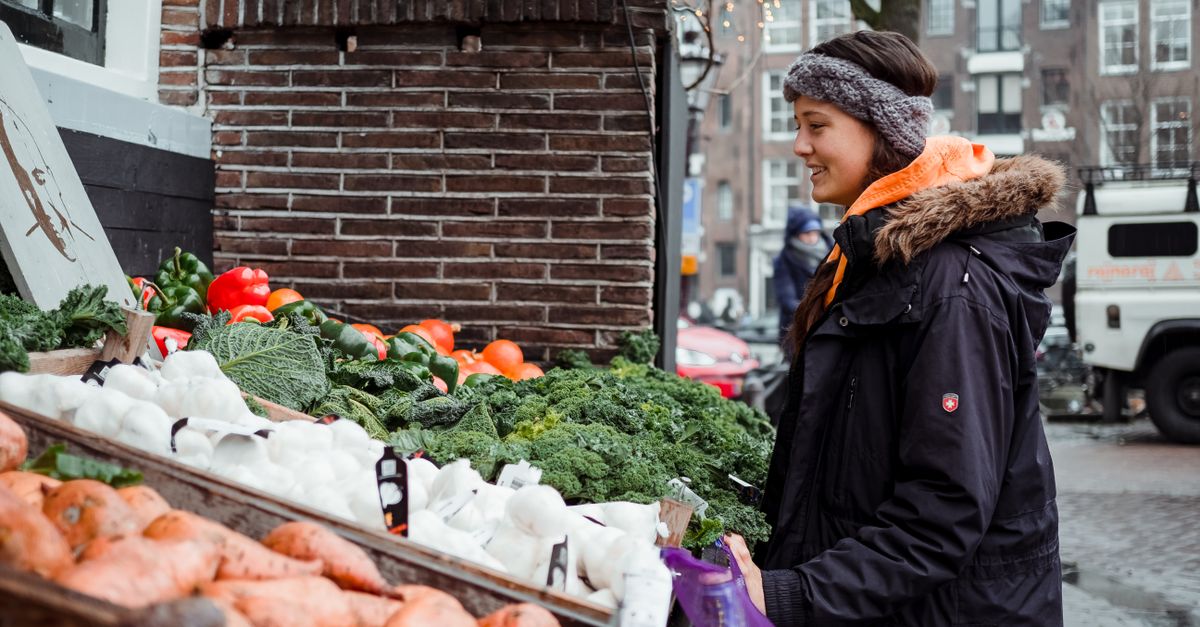 A young woman shops for fresh vegetables at an outdoor urban farmer's market in winter.