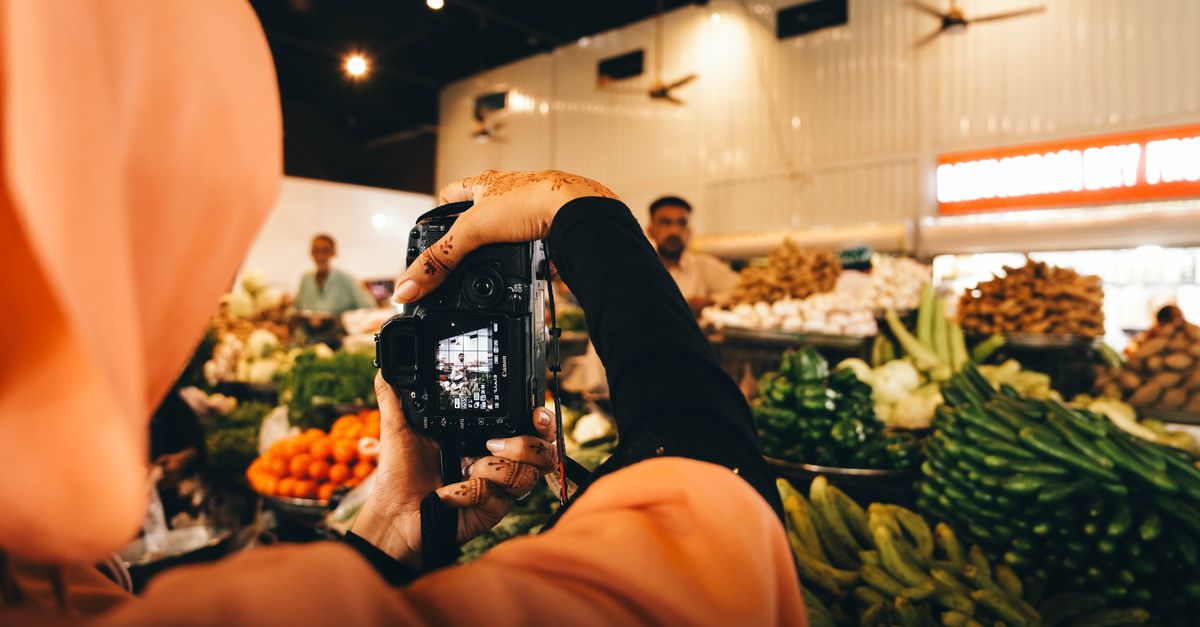 A woman photographer with henna captures vibrant vegetables at an indoor market in Sindh, Pakistan.