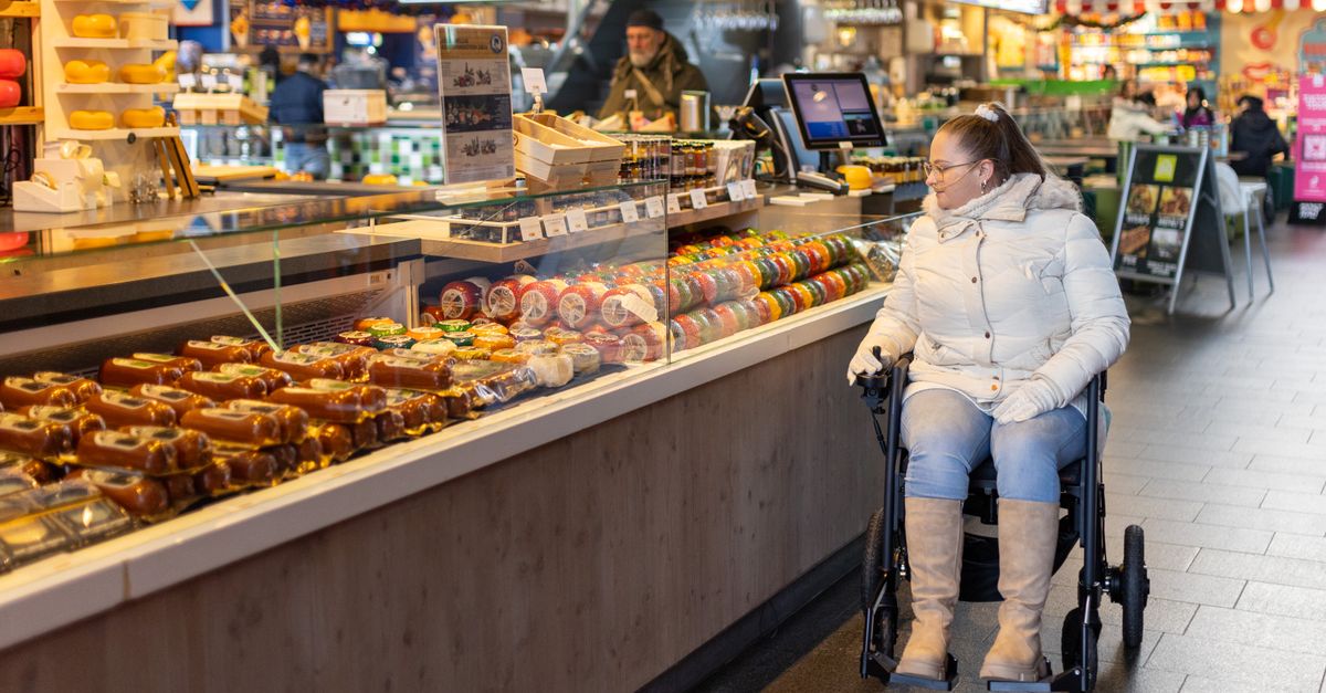 A woman in a wheelchair shops at a cheese stall inside a Rotterdam supermarket.