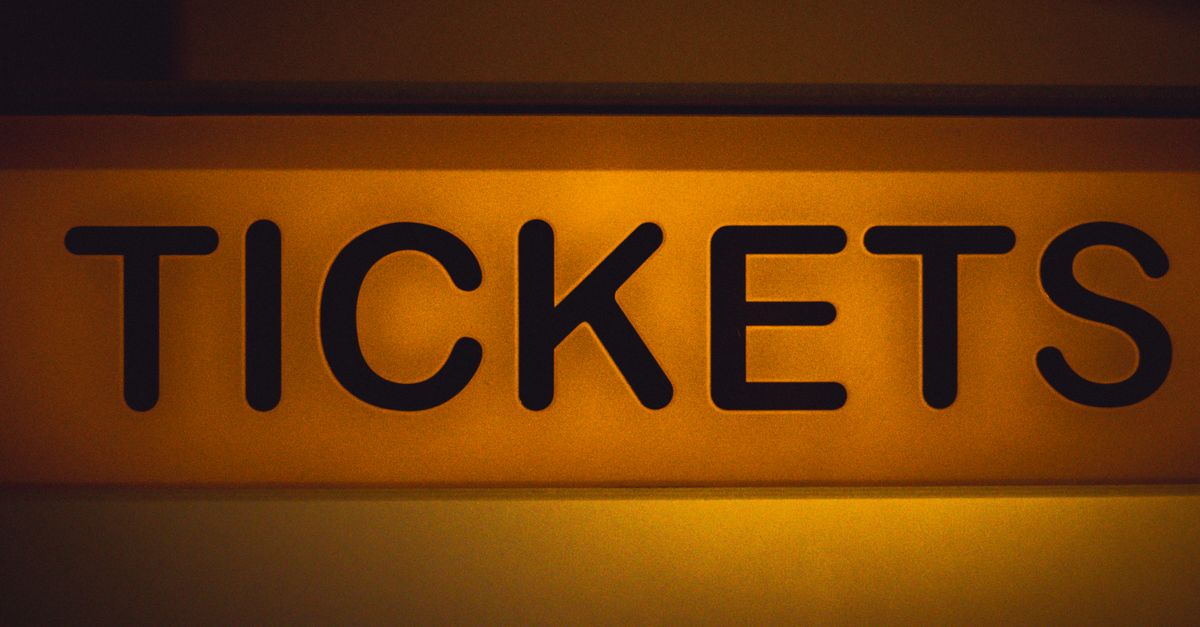 Close-up of an illuminated yellow ticket sign against a dark background.