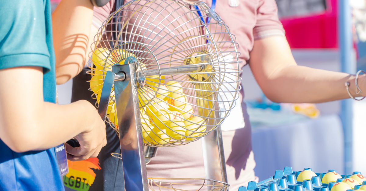 Two people engaging in a bingo game, spinning a cage in a lively, outdoor setting.