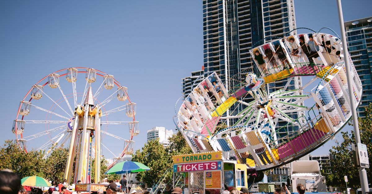 Colorful amusement park rides and bustling crowd on a sunny day.