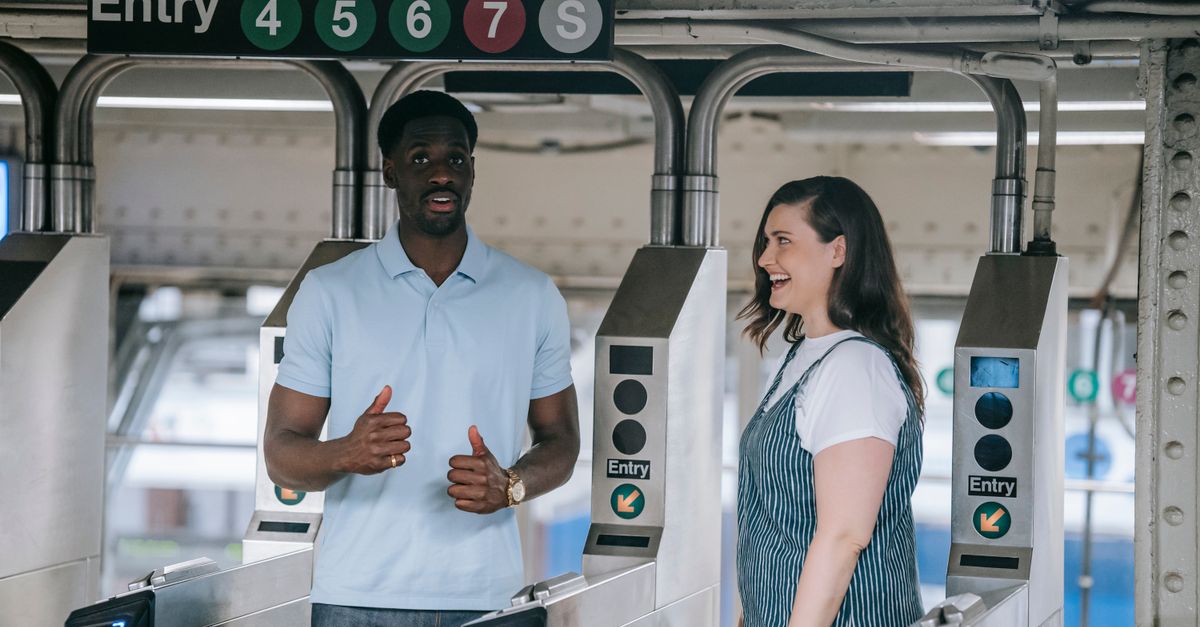 Two adults at a metro station entry turnstile having a conversation and smiling.