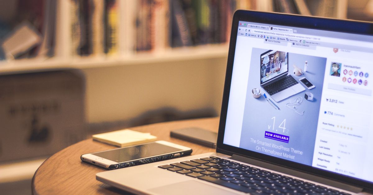 A cozy modern workspace featuring a laptop displaying a website, a smartphone, and books on shelves.