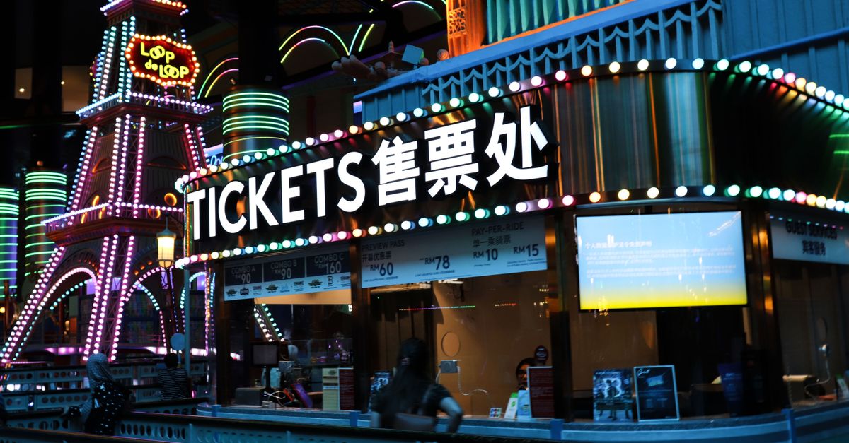 Illuminated ticket booth with vibrant neon lights at night, featuring colorful signage.