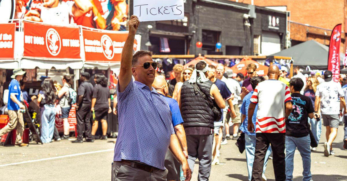 Casual man holding 'Need 2 Tickets' sign amidst crowd at Seattle event.