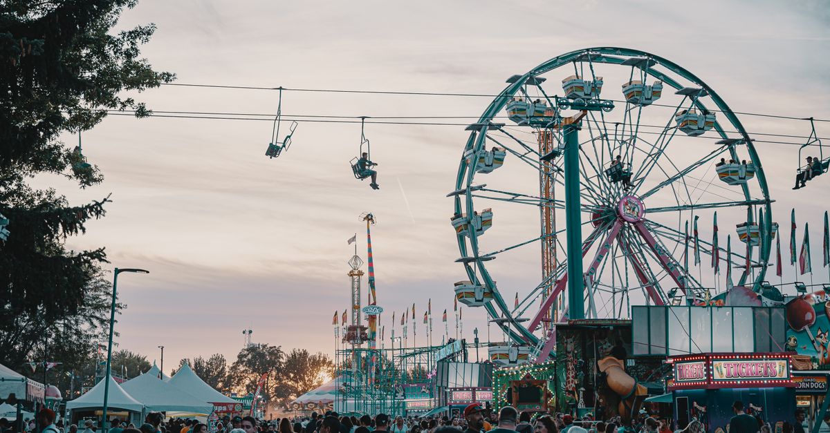 Crowd enjoying an amusement park with Ferris wheel and rides at sunset.