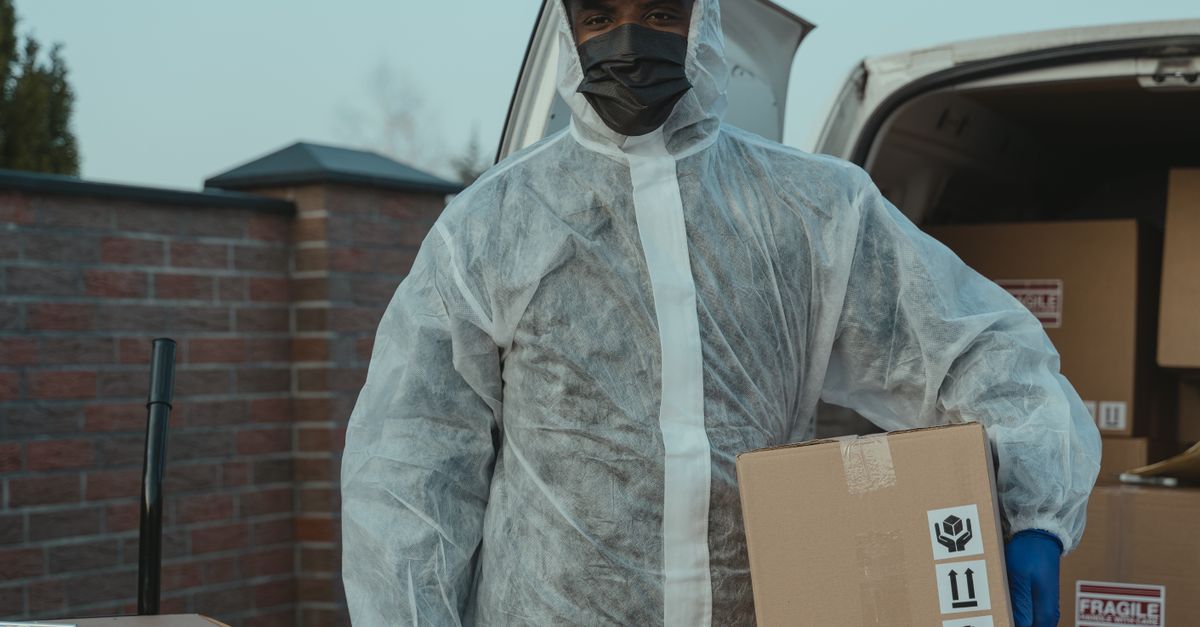 A courier wearing protective gear delivers packages from a van, ensuring safe delivery.