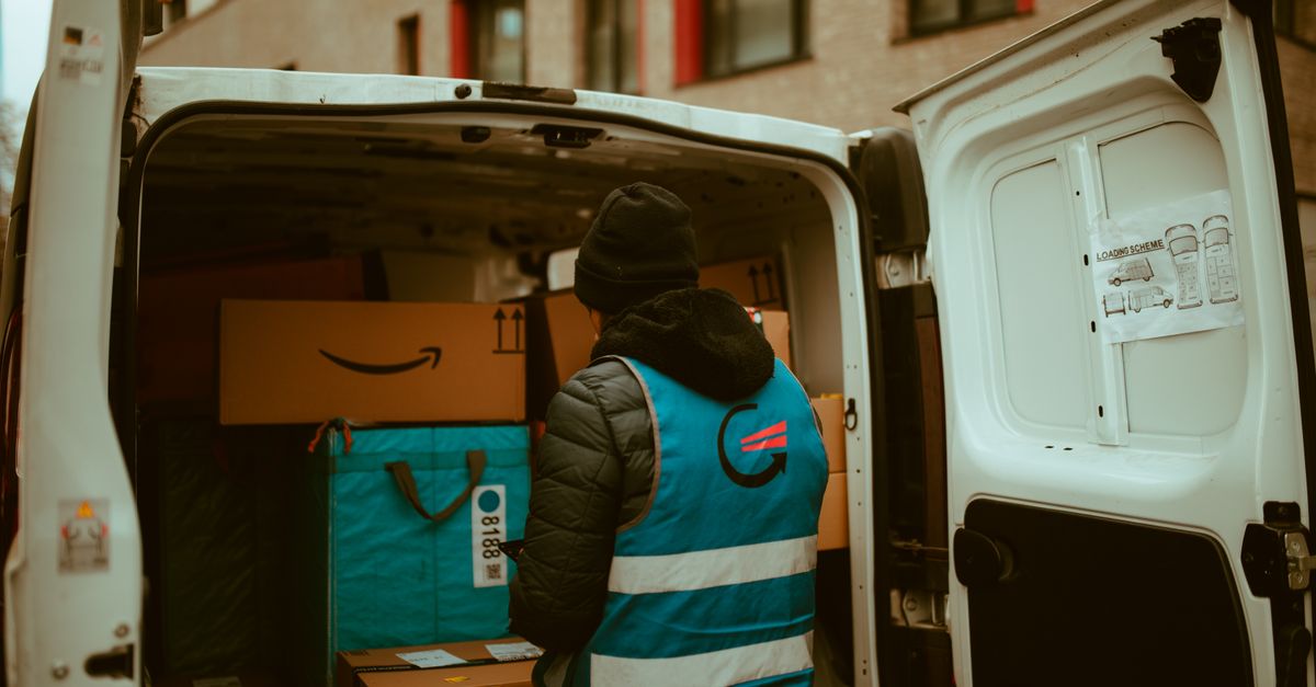 A delivery worker in a reflective vest loads packages into a van in a city setting.