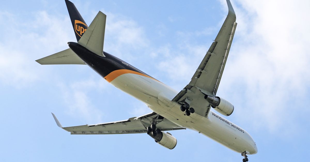 A cargo aircraft flying against a backdrop of a clear blue sky, showing its wings and landing gear.