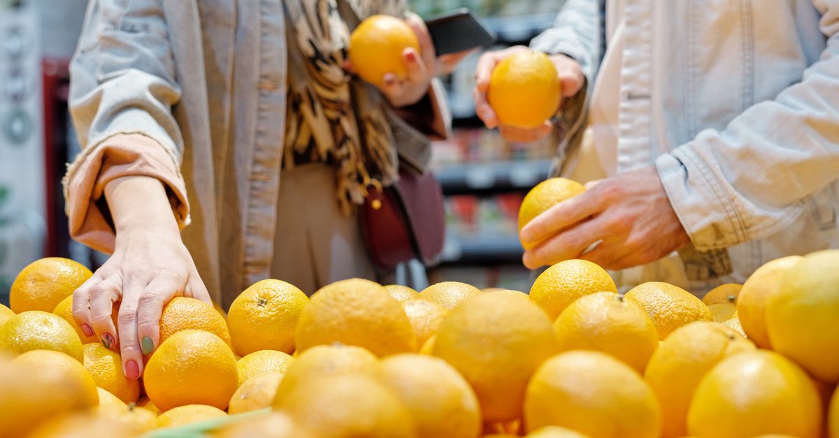Close-up of hands selecting fresh oranges in a bustling market.