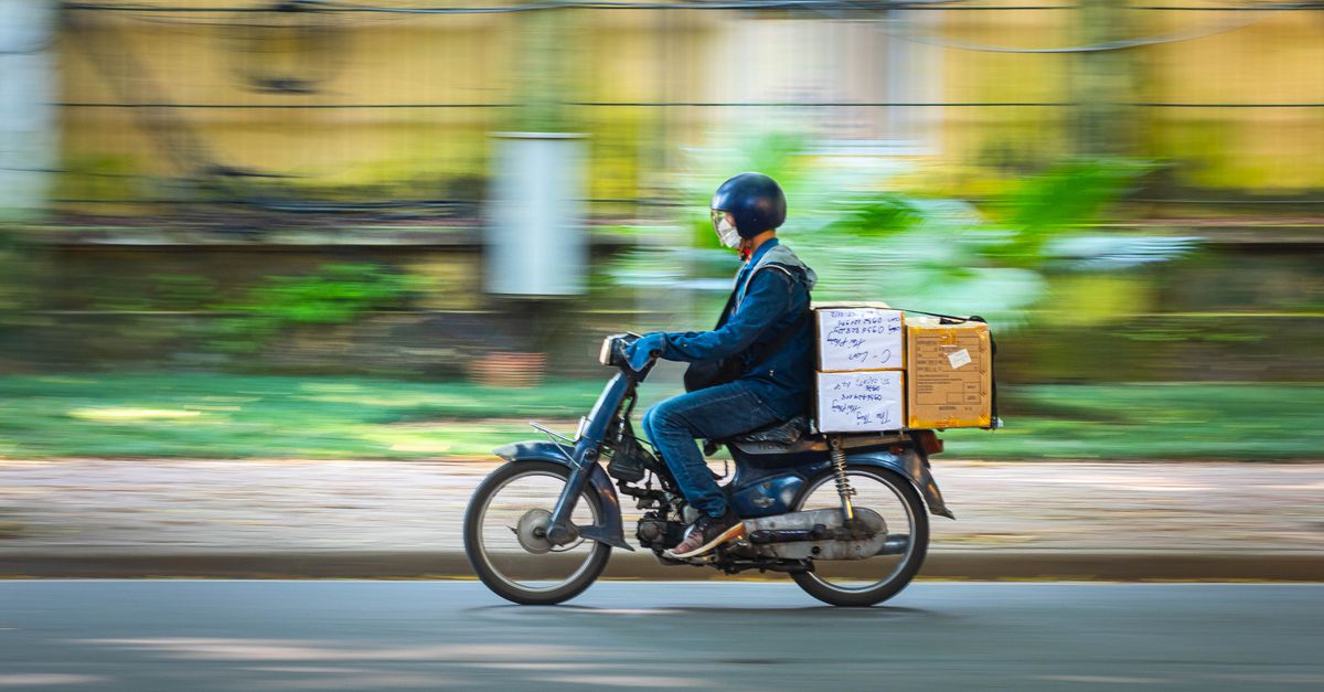 Side view of a motorcycle courier speeding down a road with packages in motion blur background.