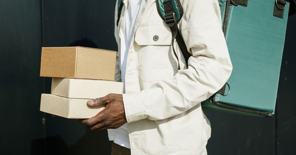Close-up of a delivery person holding cardboard packages outdoors, showcasing modern urban logistics.
