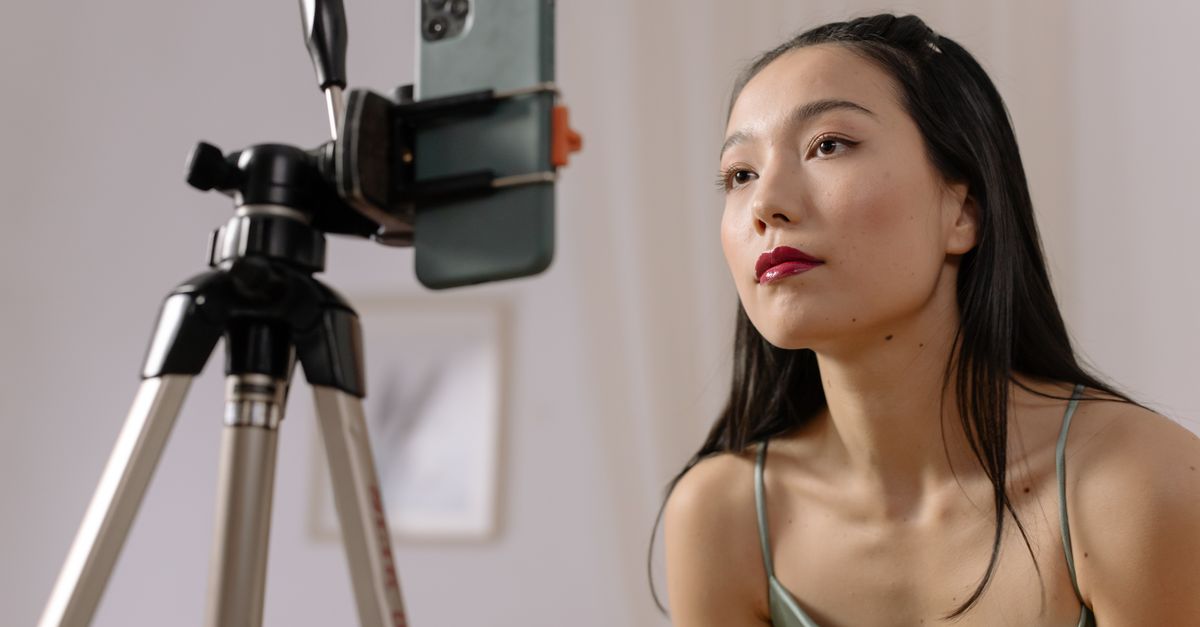 Asian woman recording a vlog indoors using a smartphone on a tripod.