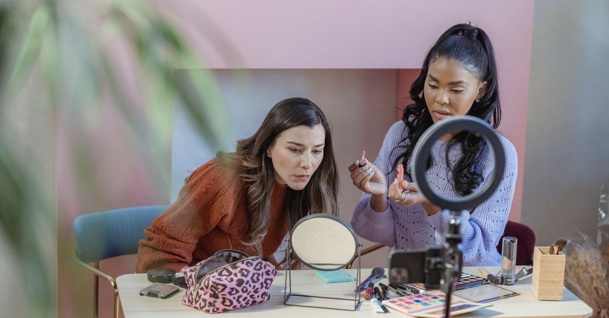 Diverse focused friends at table with eyeshadows and cosmetics near ring lamp in fashion studio