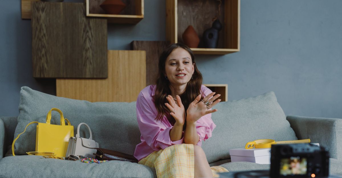 Young woman sitting on a couch, recording a fashion video blog indoors with stylish accessories and camera.