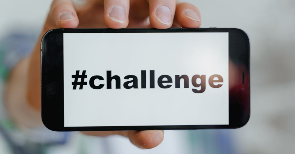 Close-up of a hand holding a smartphone displaying a '#challenge' hashtag.