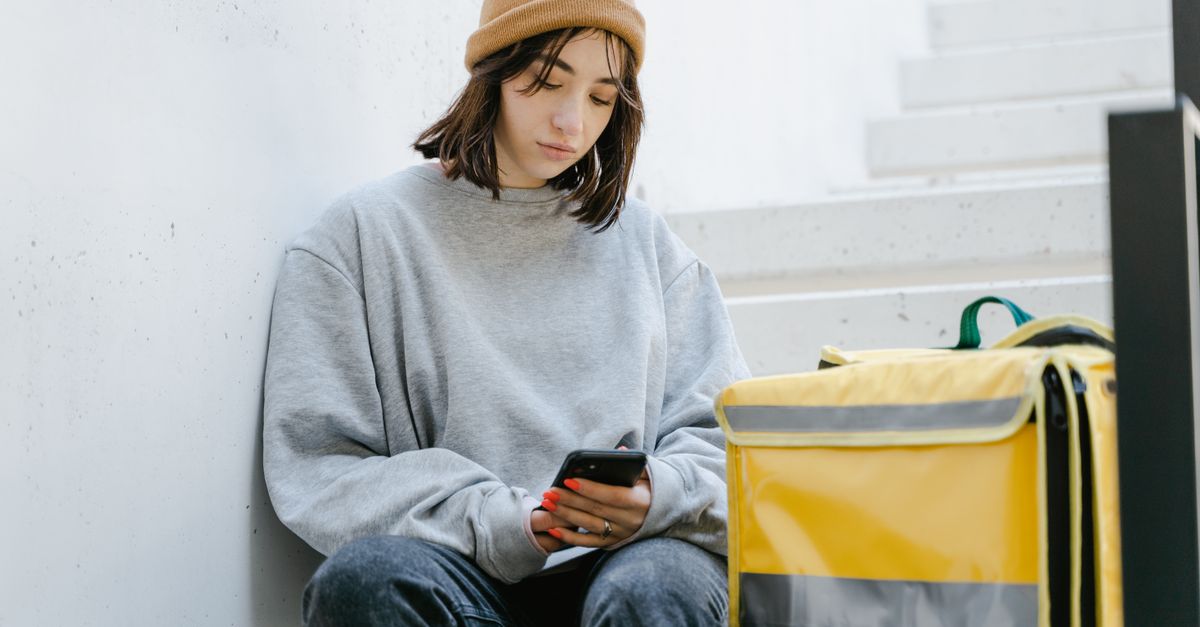 A young woman sitting on stairs using a smartphone next to a yellow delivery bag.