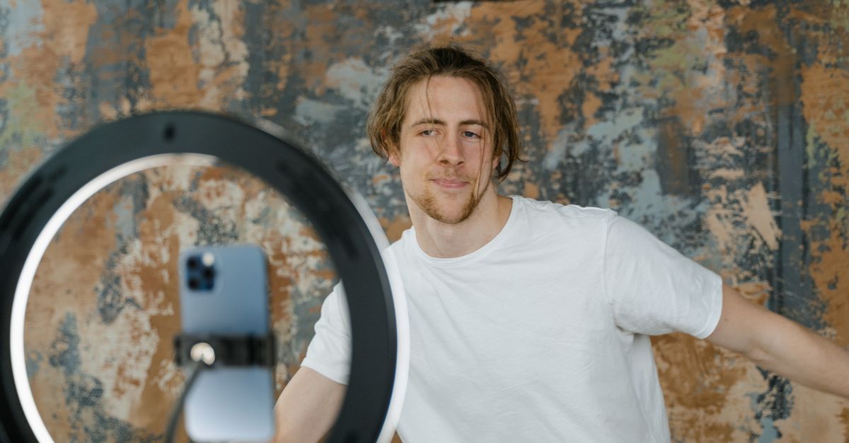 Man filming vlog with smartphone and ring light in an indoor setting. Casual attire.