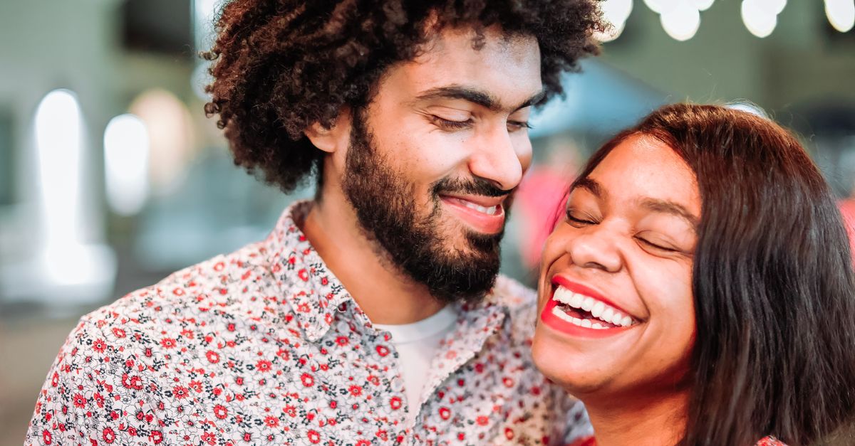 Close-up of a happy couple sharing a joyous moment with bright smiles under bokeh lights.
