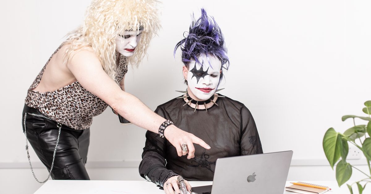 Two individuals with glam rock makeup using a laptop, blending creativity with technology.