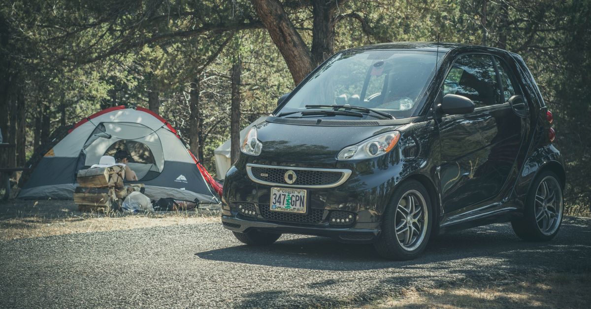 Smart car parked beside a tent in a wooded campsite, perfect for outdoor adventures.